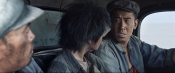 Movie still from “One Second” (2020), directed by Yimou Zhang – A man in a hat is looking at another man in a car; Close Up shot, Over the shoulder angle
