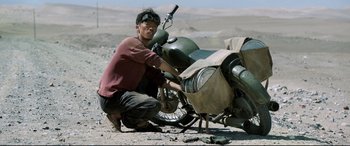 Movie still from “One Second” (2020), directed by Yimou Zhang – A man working on a motorcycle in the desert; Wide shot, High angle