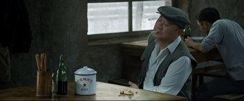 Movie still from “One Second” (2020), directed by Yimou Zhang – An older man sitting at a table with a cup of coffee; Medium shot, High angle