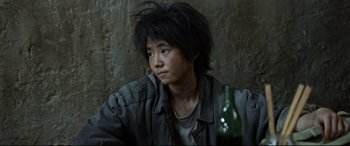 Movie still from “One Second” (2020), directed by Yimou Zhang – A person sitting in front of a wall with a bottle; Close Up shot, High angle