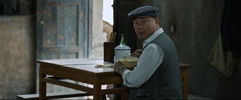 Movie still from “One Second” (2020), directed by Yimou Zhang – A man sitting at a table with a bowl of food; Medium shot, Over the shoulder angle