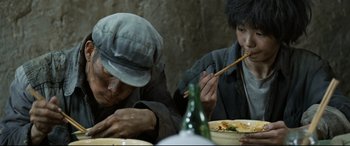 Movie still from “One Second” (2020), directed by Yimou Zhang – Two people sitting at a table eating food; Close Up shot, High angle