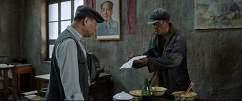 Movie still from “One Second” (2020), directed by Yimou Zhang – Two men standing at a table in front of a painting; Medium shot, Over the shoulder angle