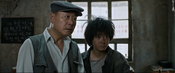 Movie still from “One Second” (2020), directed by Yimou Zhang – A man standing next to a young boy in front of a window; Close Up shot, Low angle