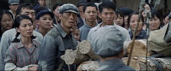 Movie still from “One Second” (2020), directed by Yimou Zhang – A group of men standing around each other holding logs; Medium shot, Over the shoulder angle