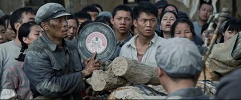 Movie still from “One Second” (2020), directed by Yimou Zhang – A group of people standing around a pile of wood; Medium shot, Over the shoulder angle