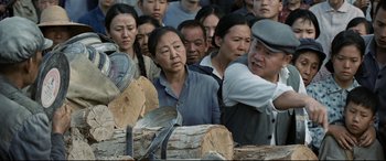 Movie still from “One Second” (2020), directed by Yimou Zhang – A group of people standing around a pile of wood; Medium shot, Over the shoulder angle