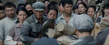 Movie still from “One Second” (2020), directed by Yimou Zhang – A group of people standing around a pile of wood; Medium shot, Over the shoulder angle
