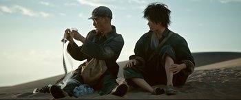 Movie still from “One Second” (2020), directed by Yimou Zhang – A man and a woman sitting on the ground; Medium shot, Low angle