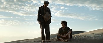Movie still from “One Second” (2020), directed by Yimou Zhang – A man and a woman sitting on the ground; Wide shot, Low angle