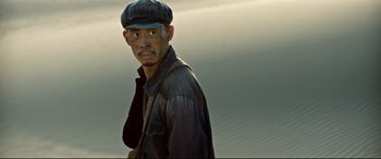Movie still from “One Second” (2020), directed by Yimou Zhang – A man wearing a hat and a leather jacket; Close Up shot, Low angle