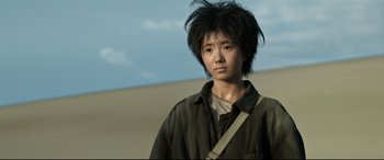 Movie still from “One Second” (2020), directed by Yimou Zhang – A young man with black hair is standing in the desert; Close Up shot, Low angle