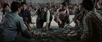 Movie still from “One Second” (2020), directed by Yimou Zhang – A group of people are gathered around a pile of debris; Wide shot, Low angle