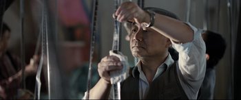 Movie still from “One Second” (2020), directed by Yimou Zhang – A man holding a tape measure in one hand and a ruler in the other hand; Medium shot, Low angle