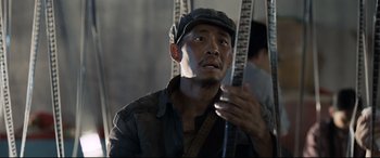 Movie still from “One Second” (2020), directed by Yimou Zhang – A man in a hat holding a pair of poles; Close Up shot, Low angle