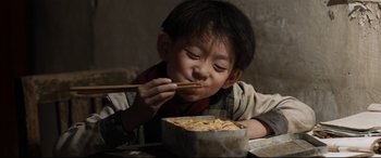 Movie still from “One Second” (2020), directed by Yimou Zhang – A young boy eating noodles with chopsticks in front of him; Medium shot, High angle