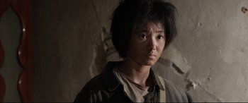 Movie still from “One Second” (2020), directed by Yimou Zhang – A young person with short black hair is looking at the camera; Close Up shot, Over the shoulder angle