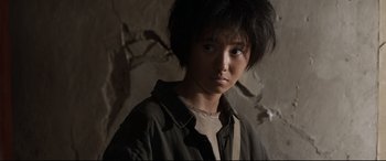 Movie still from “One Second” (2020), directed by Yimou Zhang – A young man with a black jacket and a white t - shirt; Close Up shot, Over the shoulder angle