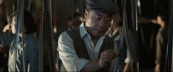 Movie still from “One Second” (2020), directed by Yimou Zhang – A man wearing a hat and a white button up shirt; Medium shot, Low angle