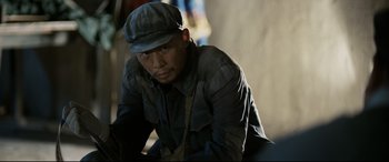 Movie still from “One Second” (2020), directed by Yimou Zhang – A man wearing a hat and sitting on the ground; Medium shot, Over the shoulder angle