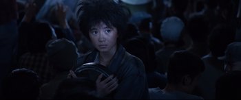 Movie still from “One Second” (2020), directed by Yimou Zhang – A person with a black wig is holding a black object; Close Up shot, Over the shoulder angle