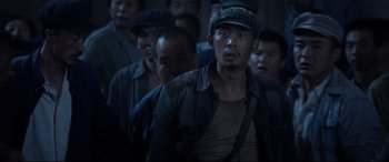 Movie still from “One Second” (2020), directed by Yimou Zhang – A group of men standing next to each other in a dark room; Medium shot, Low angle