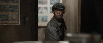 Movie still from “One Second” (2020), directed by Yimou Zhang – A man wearing a hat and jacket in a room; Medium shot, Over the shoulder angle