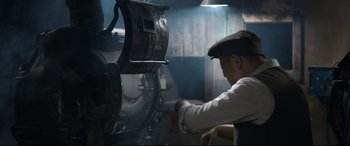 Movie still from “One Second” (2020), directed by Yimou Zhang – A man sitting in front of a machine in a room; Medium shot, Low angle