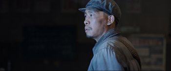 Movie still from “One Second” (2020), directed by Yimou Zhang – A man wearing a hat looking to his left; Close Up shot, Low angle
