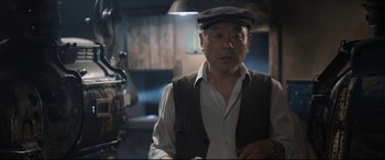 Movie still from “One Second” (2020), directed by Yimou Zhang – An older man wearing a hat and vest; Medium shot, Low angle