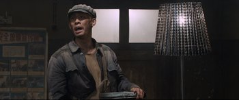 Movie still from “One Second” (2020), directed by Yimou Zhang – A man wearing a hat and holding a laptop; Medium shot, Low angle