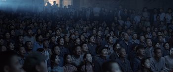 Movie still from “One Second” (2020), directed by Yimou Zhang – A group of people sitting in a room watching something; Wide shot, High angle