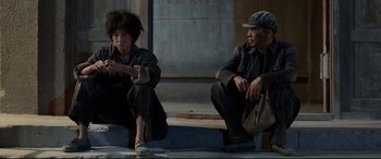 Movie still from “One Second” (2020), directed by Yimou Zhang – A man and a woman sitting next to each other on steps; Medium shot, Low angle