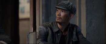 Movie still from “One Second” (2020), directed by Yimou Zhang – A man wearing a hat and jacket looking off into the distance; Close Up shot, Low angle