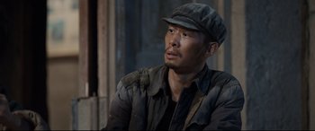 Movie still from “One Second” (2020), directed by Yimou Zhang – A man wearing a hat and jacket sitting in a room; Close Up shot, High angle
