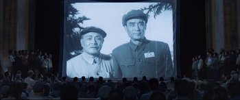 Movie still from “One Second” (2020), directed by Yimou Zhang – A large screen showing two men standing next to each other; Medium shot, Low angle