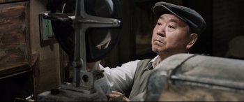 Movie still from “One Second” (2020), directed by Yimou Zhang – A man in a hat is looking into a mirror; Close Up shot, Low angle