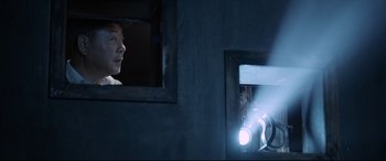 Movie still from “One Second” (2020), directed by Yimou Zhang – A man looking out a window in a room; Medium shot, Low angle