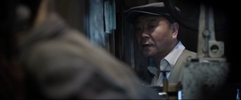 Movie still from “One Second” (2020), directed by Yimou Zhang – A man wearing a hat looking out a window; Close Up shot, Over the shoulder angle