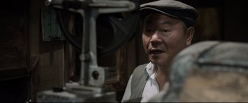 Movie still from “One Second” (2020), directed by Yimou Zhang – An older man wearing a hat looking at a machine; Close Up shot, Low angle