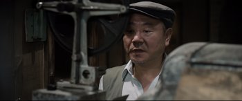 Movie still from “One Second” (2020), directed by Yimou Zhang – An asian man wearing a hat looking into a machine; Close Up shot, Low angle