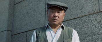 Movie still from “One Second” (2020), directed by Yimou Zhang – An older man wearing a hat and a vest; Close Up shot, Low angle