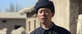 Movie still from “One Second” (2020), directed by Yimou Zhang – A man wearing a blue hat and a black jacket; Close Up shot, Low angle