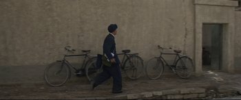 Movie still from “One Second” (2020), directed by Yimou Zhang – A man walking down a street past a row of parked bicycles; Wide shot, Low angle