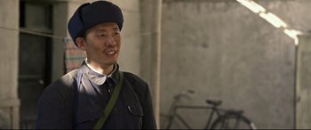 Movie still from “One Second” (2020), directed by Yimou Zhang – A man wearing a hat standing next to a bicycle; Close Up shot, Over the shoulder angle