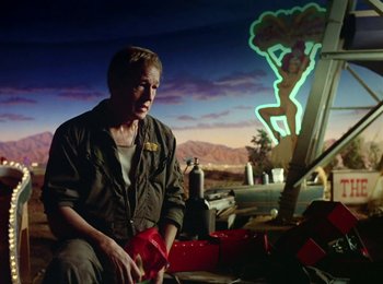 Movie still from “One from the Heart” (1981), directed by Francis Ford Coppola – A man sitting on the ground in front of a neon sign; Medium shot, Low angle