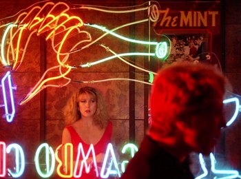 Movie still from “One from the Heart” (1981), directed by Francis Ford Coppola – A woman in a red dress in front of a neon sign; Medium shot, Over the shoulder angle