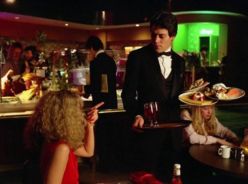 Movie still from “One from the Heart” (1981), directed by Francis Ford Coppola – A man in a suit holding a tray with a glass of red wine on top of it; Medium shot, Over the shoulder angle