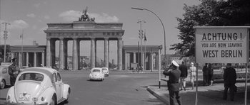 Movie still from “One, Two, Three” (1961), directed by Billy Wilder – An old photo of a woman taking a picture in front of the brandenburg gate; Wide shot, Low angle