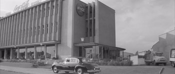 Movie still from “One, Two, Three” (1961), directed by Billy Wilder – An old car is parked in front of a building; Extreme Wide shot, Low angle